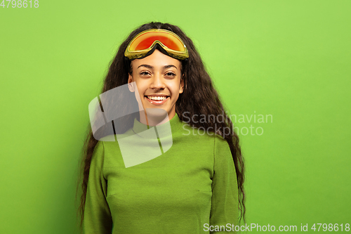 Image of African-american young woman\'s portrait in ski mask on green background