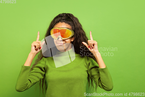 Image of African-american young woman\'s portrait in ski mask on green background