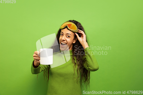 Image of African-american young woman\'s portrait in ski mask on green background