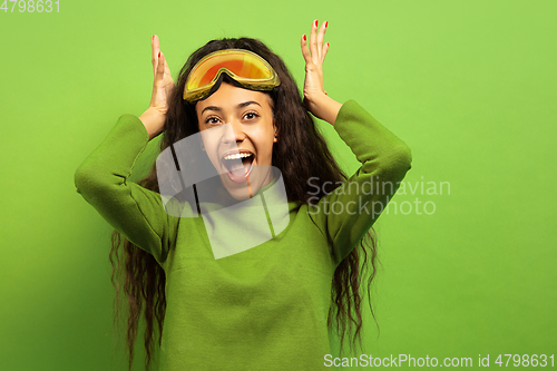 Image of African-american young woman\'s portrait in ski mask on green background