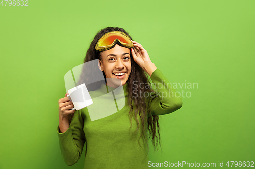 Image of African-american young woman\'s portrait in ski mask on green background