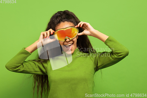 Image of African-american young woman\'s portrait in ski mask on green background