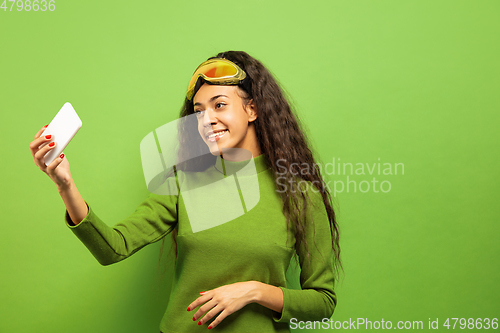 Image of African-american young woman\'s portrait in ski mask on green background
