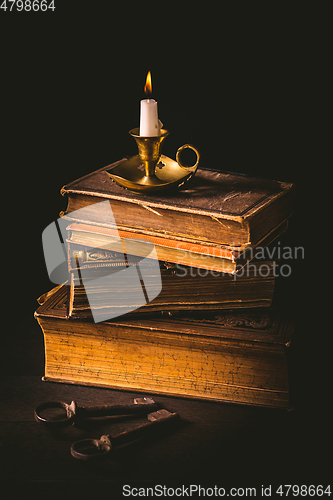 Image of Pile of old antique books with candle in vintage style on black background