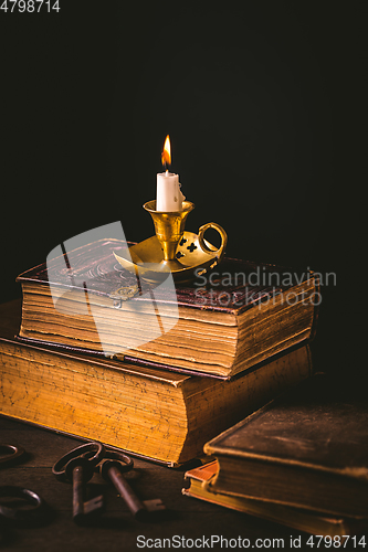 Image of Pile of old antique books with candle in vintage style on black background