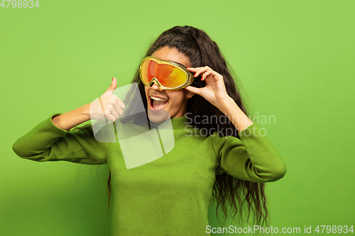 Image of African-american young woman\'s portrait in ski mask on green background