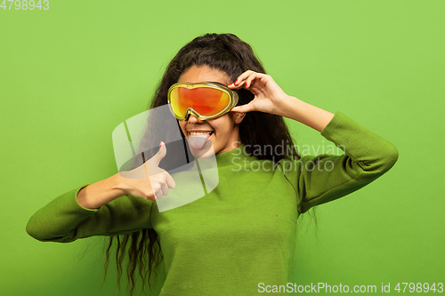 Image of African-american young woman\'s portrait in ski mask on green background