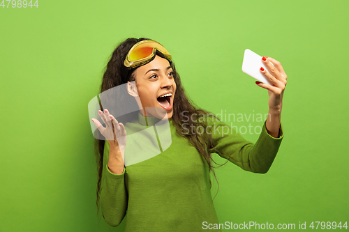 Image of African-american young woman\'s portrait in ski mask on green background