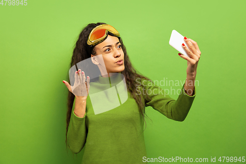 Image of African-american young woman\'s portrait in ski mask on green background