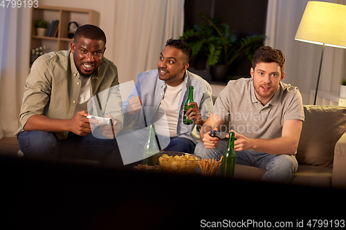 Image of happy friends playing video games at home at night