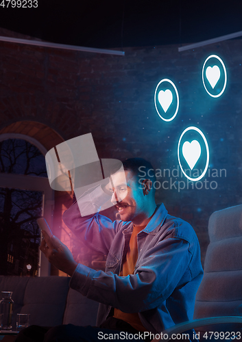 Image of Man using gadget and receive neon notifications at home at night