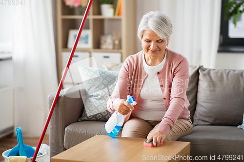 Image of senior woman with detergent cleaning table at home