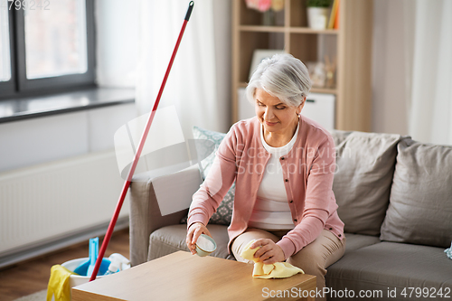 Image of senior woman cleaning table with soda at home