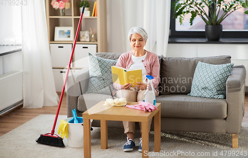 Image of senior woman reading book after home cleaning