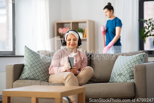 Image of old woman in headphones with smartphone at home