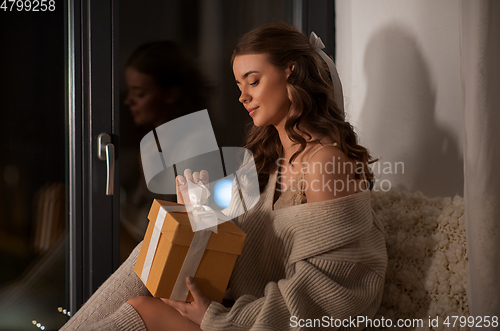 Image of woman with gift box at home at night