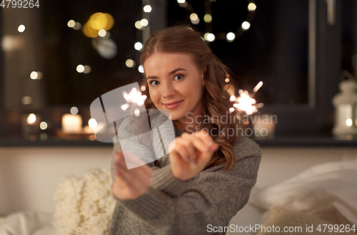 Image of happy young woman with sparklers in bed at home