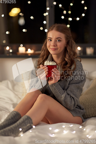 Image of happy woman holding mug with whipped cream in bed