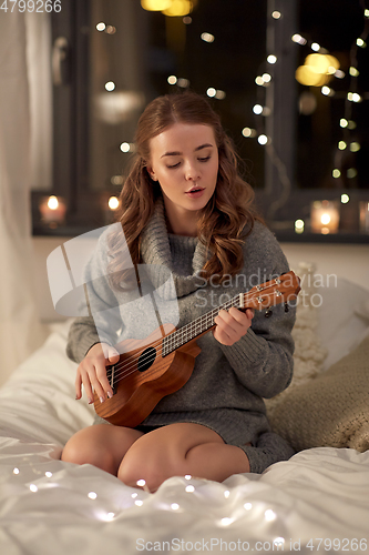 Image of happy young woman playing guitar in bed at home