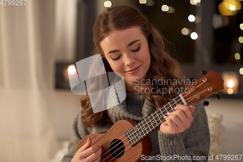 Image of happy young woman playing ukulele guitar at home