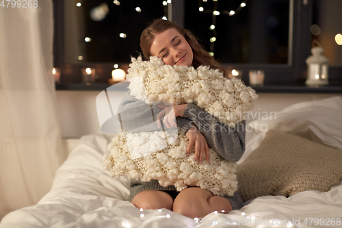 Image of happy young woman with soft pillow in bed at home