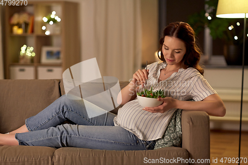 Image of happy smiling pregnant woman eating salad at home