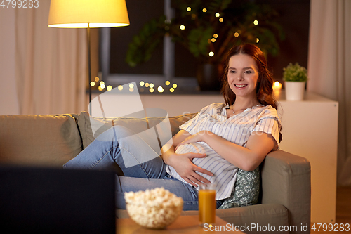 Image of happy smiling pregnant woman watching tv at home