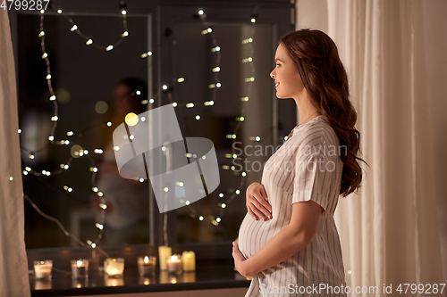 Image of happy pregnant woman looking out window at home