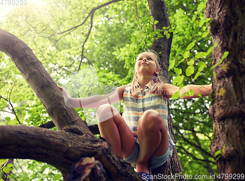 Image of happy girl climbing up tree in summer park