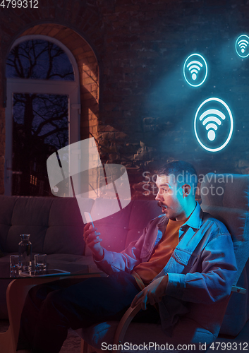 Image of Man using gadget and receive neon notifications at home at night