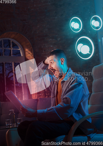 Image of Man using gadget and receive neon notifications at home at night