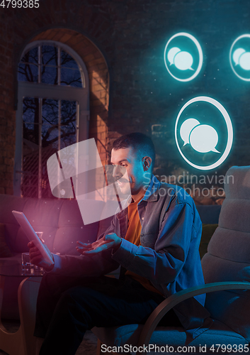 Image of Man using gadget and receive neon notifications at home at night