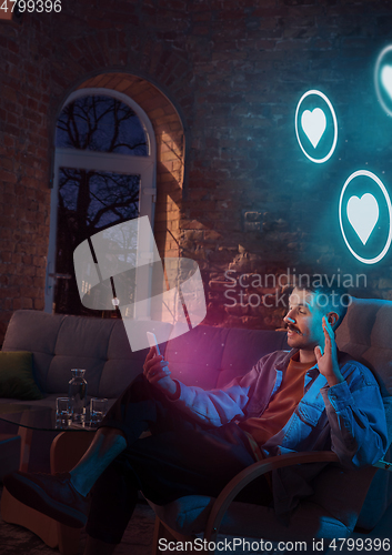 Image of Man using gadget and receive neon notifications at home at night