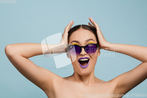 Image of Portrait of beautiful young woman with bright make-up isolated on blue studio background