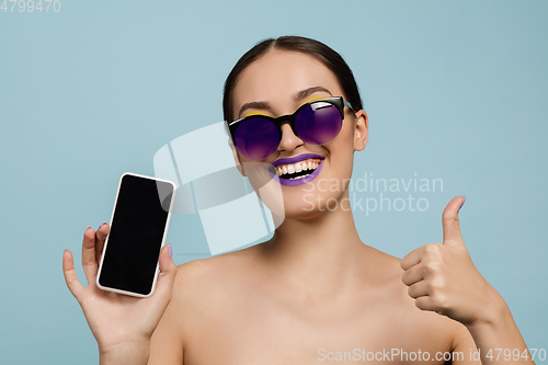 Image of Portrait of beautiful young woman with bright make-up isolated on blue studio background