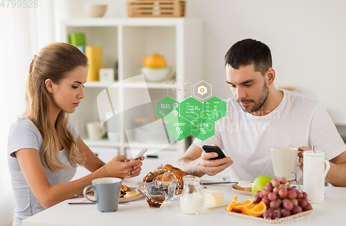 Image of couple with smartphones having breakfast at home