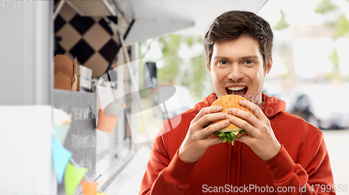 Image of happy young man eating hamburger at food truck