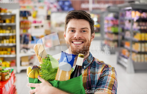 Image of smiling young man with food in bag at supermarket