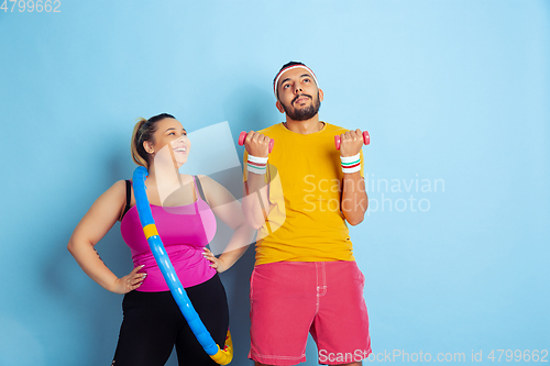 Image of Young pretty caucasian couple in bright clothes training on blue background