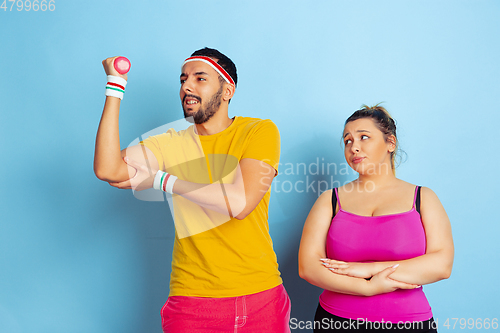 Image of Young pretty caucasian couple in bright clothes training on blue background