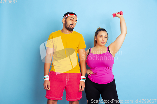 Image of Young pretty caucasian couple in bright clothes training on blue background