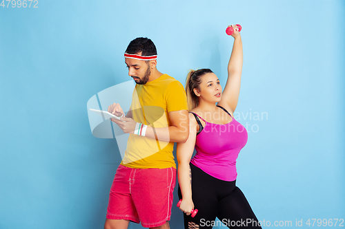 Image of Young pretty caucasian couple in bright clothes training on blue background
