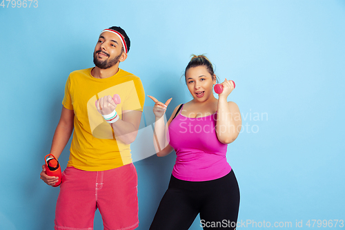 Image of Young pretty caucasian couple in bright clothes training on blue background