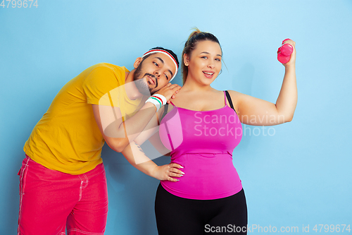 Image of Young pretty caucasian couple in bright clothes training on blue background