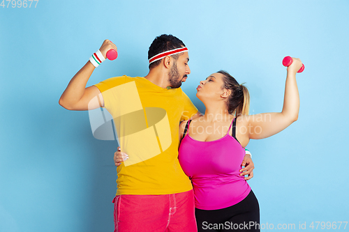 Image of Young pretty caucasian couple in bright clothes training on blue background