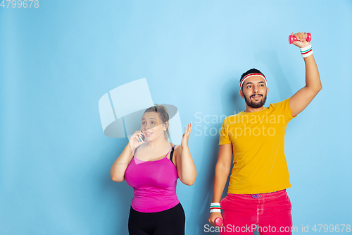 Image of Young pretty caucasian couple in bright clothes training on blue background