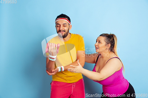 Image of Young pretty caucasian couple in bright clothes training on blue background