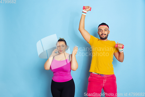 Image of Young pretty caucasian couple in bright clothes training on blue background
