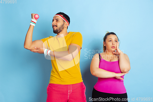 Image of Young pretty caucasian couple in bright clothes training on blue background