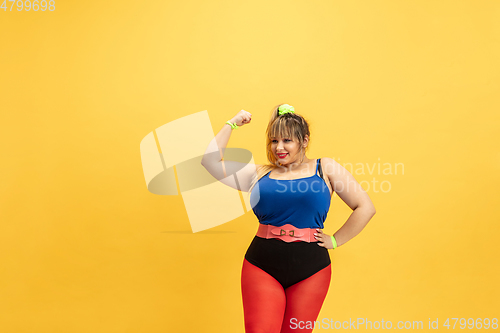 Image of Young caucasian plus size female model\'s training on yellow background